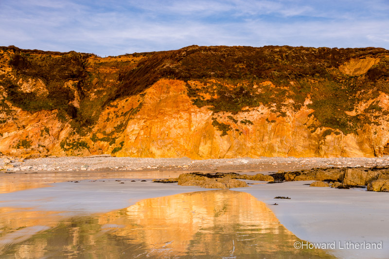 Golden cliffs reflecting in wet sand on the beach at Church Bay, Anglesey, North Wales