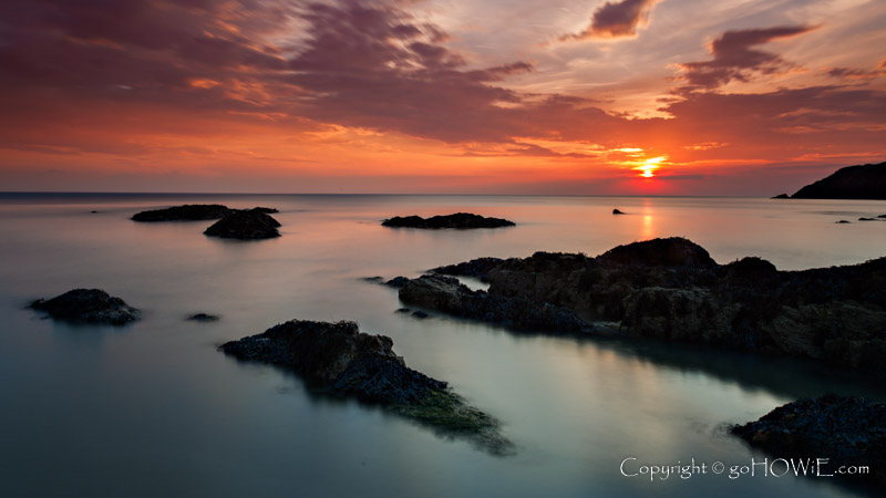 Rocks partially submerged by a rising tide on the beach at Church Bay, Anglesey, North Wales, at sunset