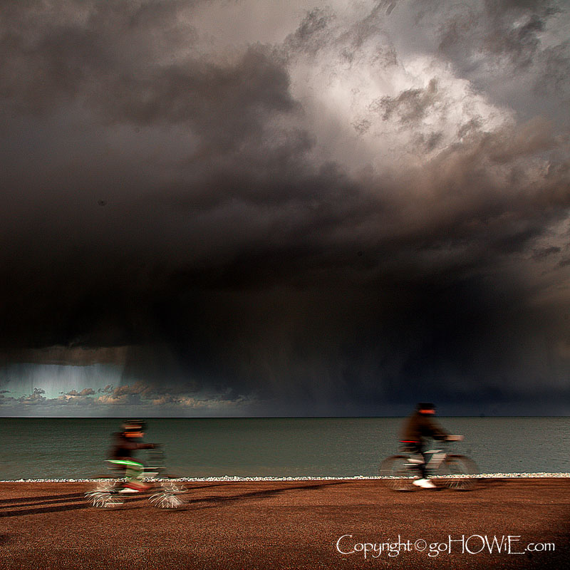 Cyclists on Llandudno East Shore promenade with storm clouds, North Wales coast