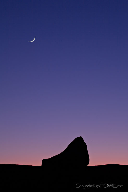 A crescent moon over a silhouetted rock at dusk, Moel Famau, North Wales
