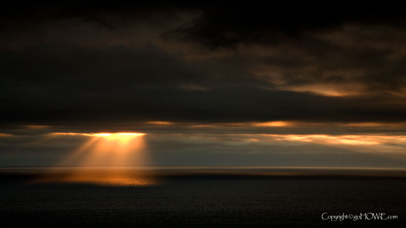 Photo of sun rays shining through heavy cloud onto the sea