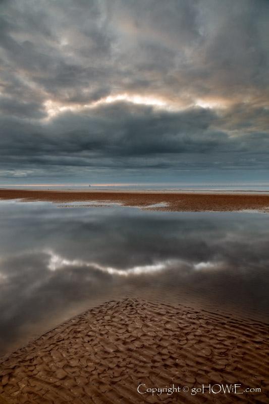 Beach at Rhyl on the North Wales coast, with cloud patterns reflecting in a tidal pool