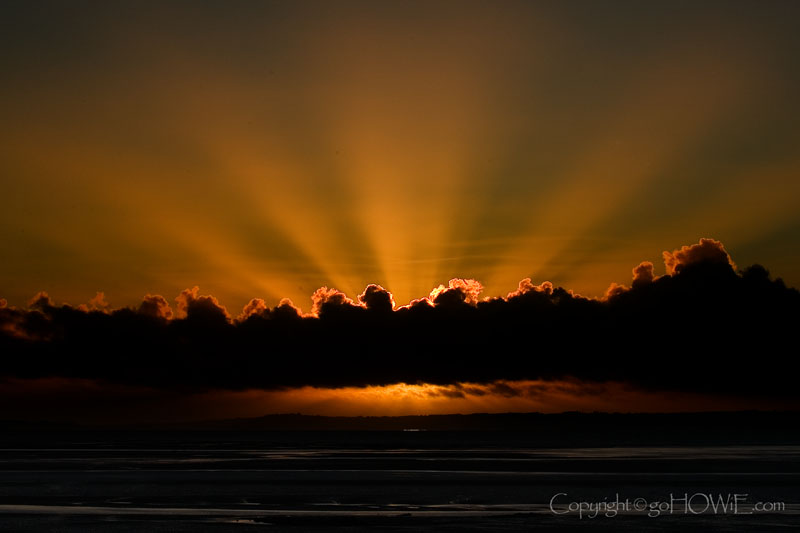 The sun's rays fanning out from behind a bank of cloud at sunset over the Conwy estuary, taken from the West Shore, Llandudno on the North Wales coast