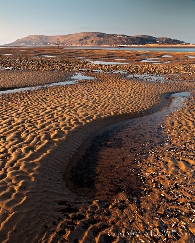 The beach at Conwy Morfa on the North Wales coast at low tide showing contours and patterns in the sand and with the Great Orme headland in the background