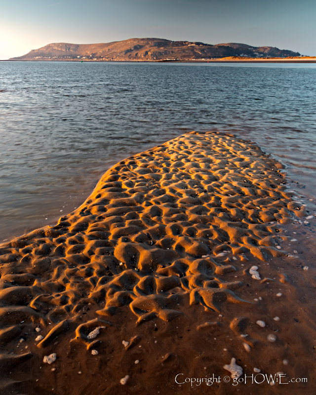 The beach at Conwy Morfa on the North Wales coast at low tide showing contours and patterns in the sand and with the Great Orme headland in the background