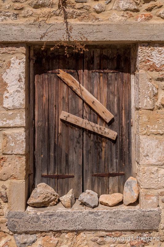 Old window with closed wooden shutters set in a stone wall at Old Hersonissos on the Mediterranean island of Crete
