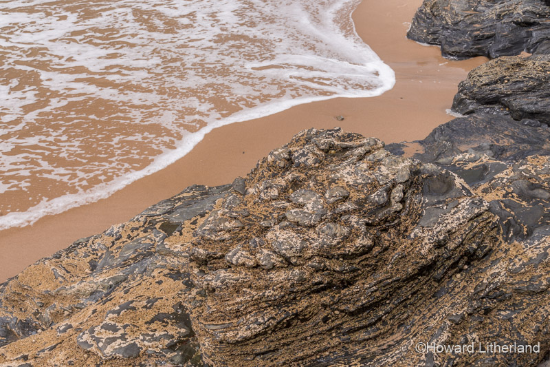 Sand, rock and a wave on the beach at Llangrannog on the Ceredigion coast, Mid Wales