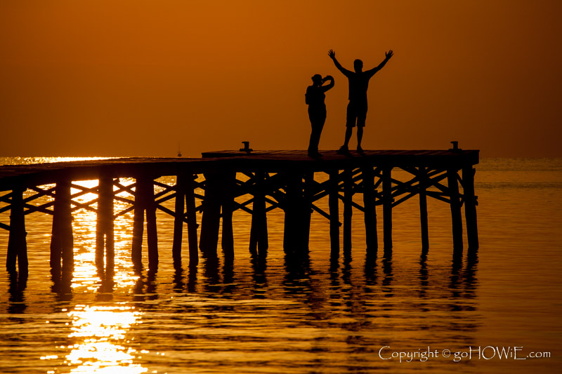 two tourists photographing each other on a jetty at sunrise, Alcudia Bay, Mallorca