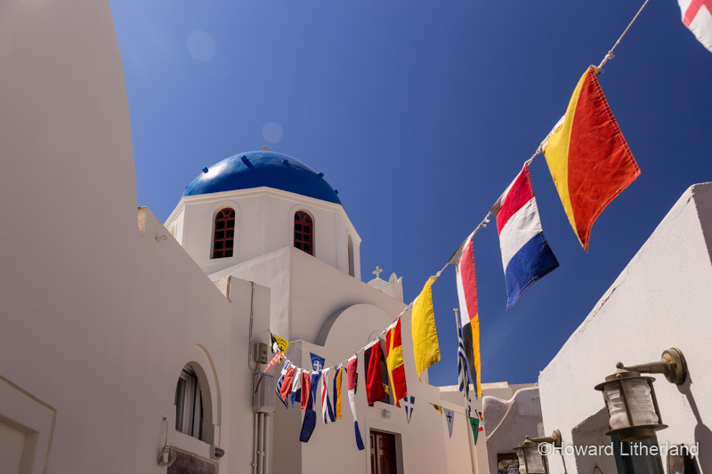 Church with blue dome and flags at Oia on the island of Santorini