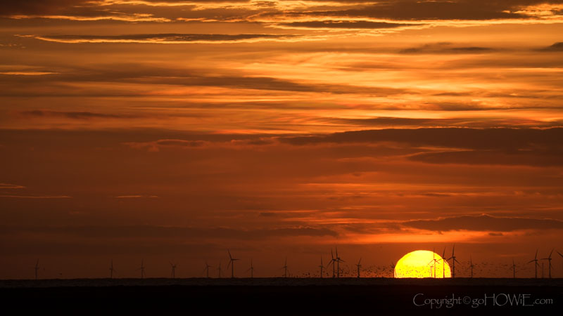 The sun setting behind the Colwyn Bay windfarm, North Wales, photographed from the Marine Lake, West Kirby, Wirral