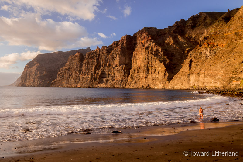 A woman in the surf below the sea cliffs on the beach at Los Gigantes on Tenerife in the Canary Islands